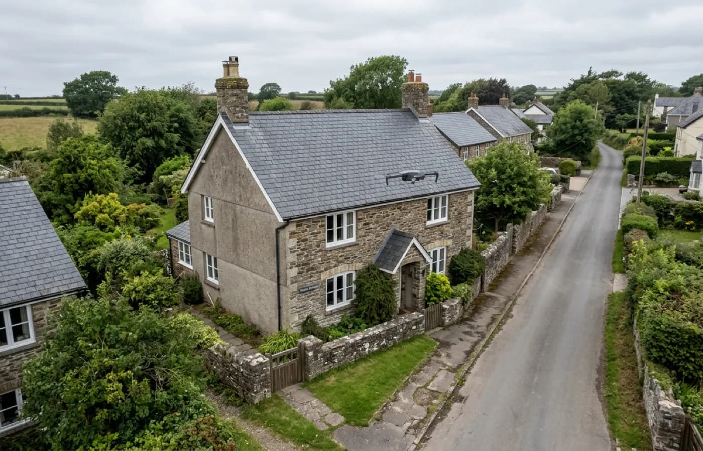 A single Devon house on an ordinary residential street with a survey drone hovering above the roof, no scaffolding or ladder in shot